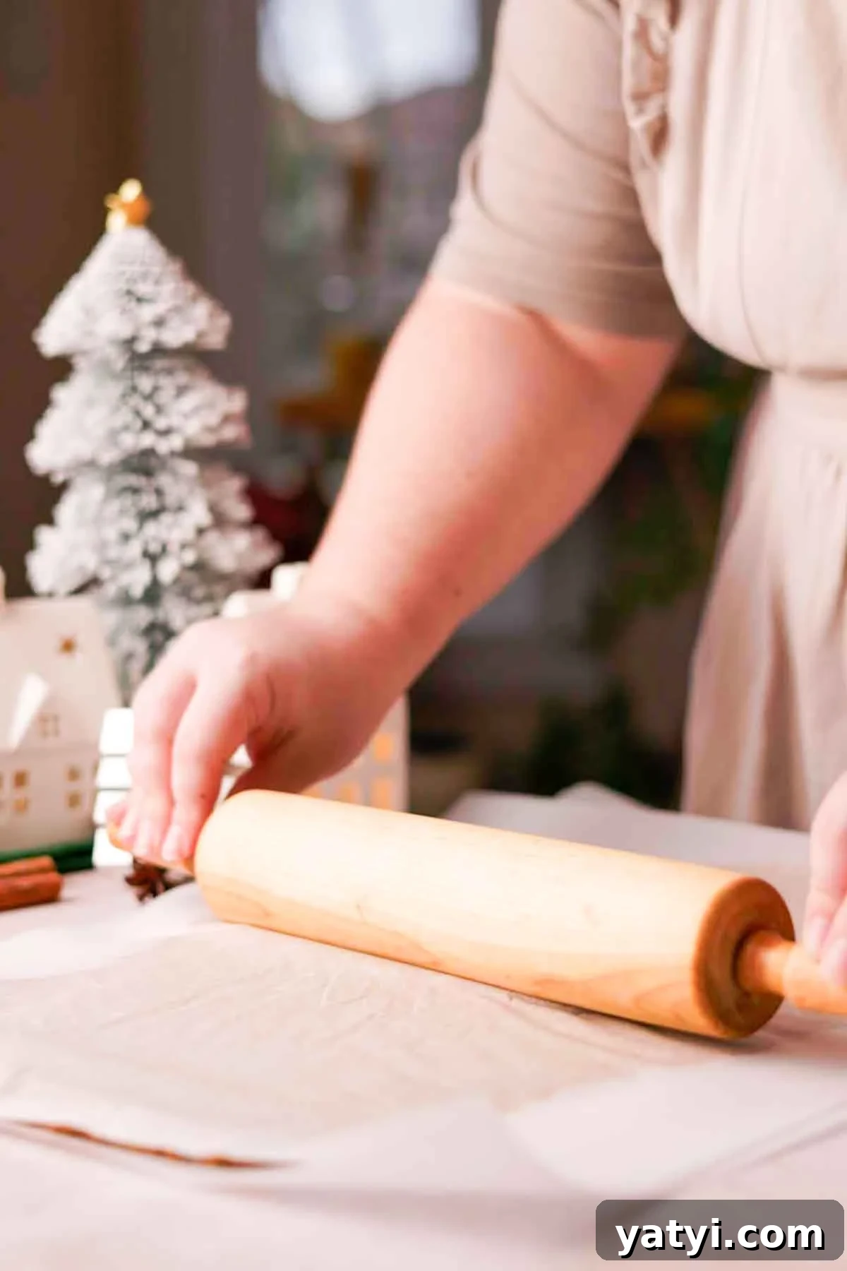 rolling out gingerbread dough between two sheets of parchment paper with wood rolling pin