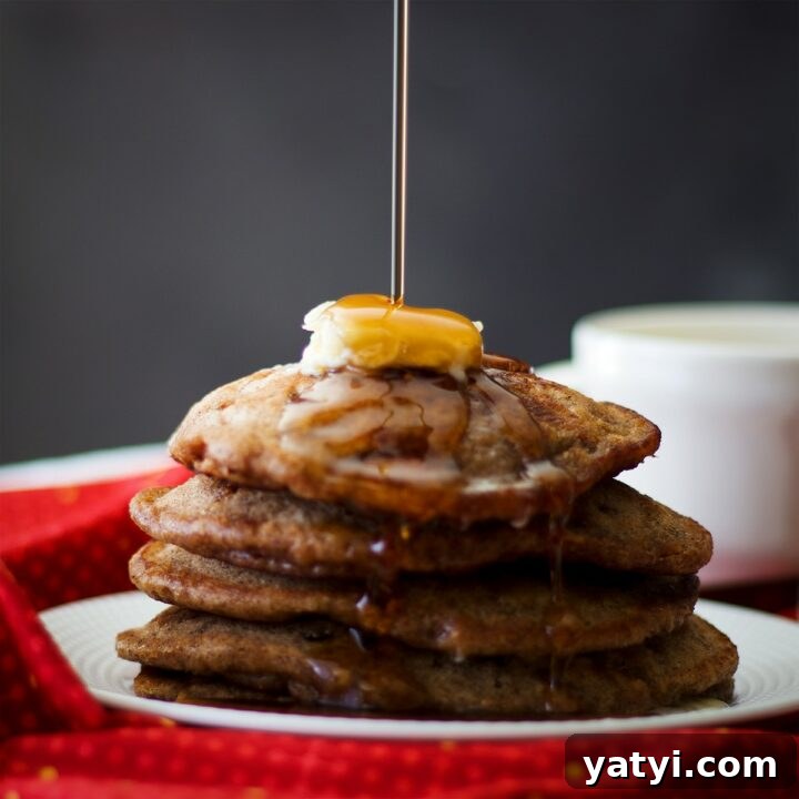 Pouring maple syrup over a stack of apple cinnamon pancakes.