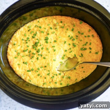 crock pot corn casserole in a slow cooker, with a spoon.