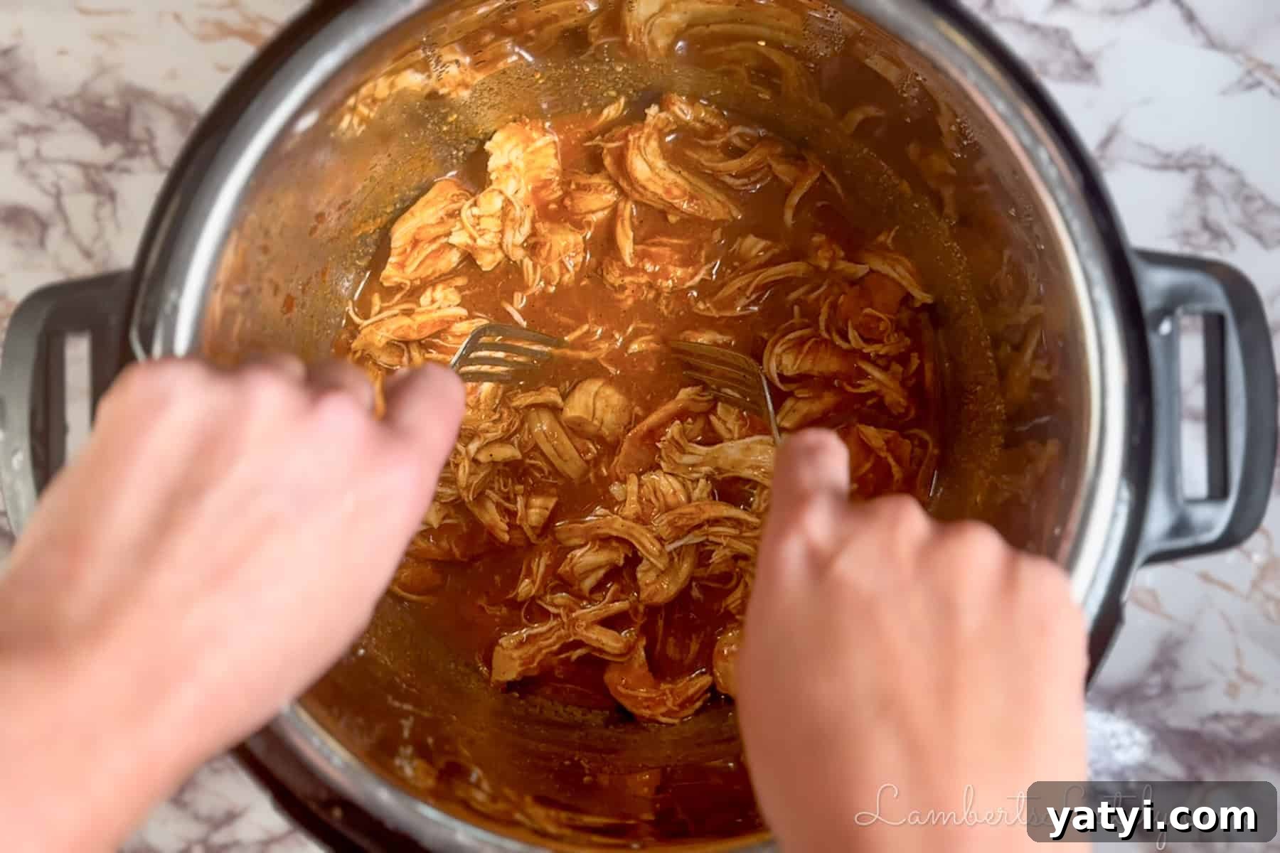 shredding cooked chicken in an instant pot with forks.