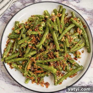 crack green beans, covered in a bacon sauce, on a plate.