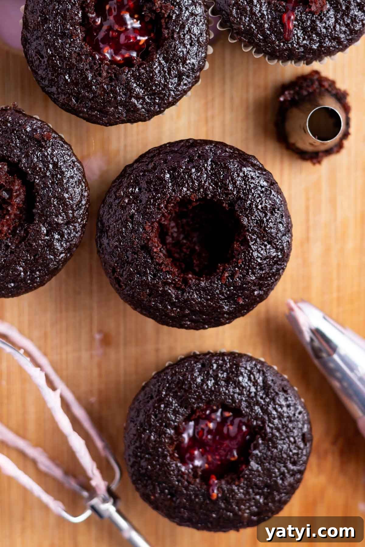 Moist Chocolate Cupcakes with Raspberry Filling and Ganache 14 chocolate cupcakes on a cutting board with the centers removed; some are filled with raspberry jam