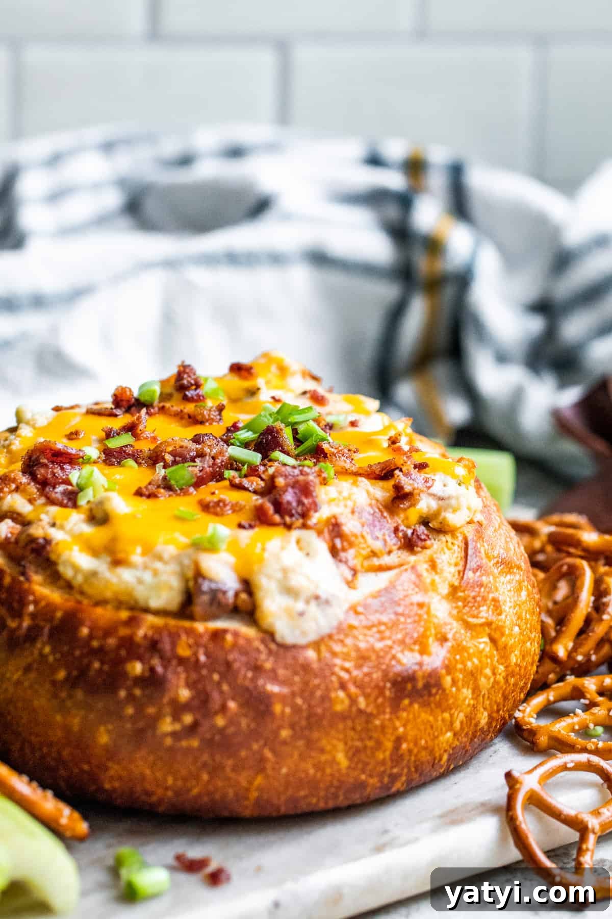 Baked Bacon and Cheese Dip Served in a Warm Bread Bowl 2 Bacon cheese dip in a bread bowl with dippers on a white counter.