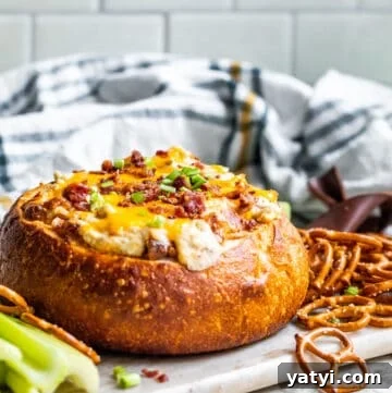 Baked Bacon and Cheese Dip Served in a Warm Bread Bowl 13 Baked dip in a bread bowl on white counter sitting on serving tray.