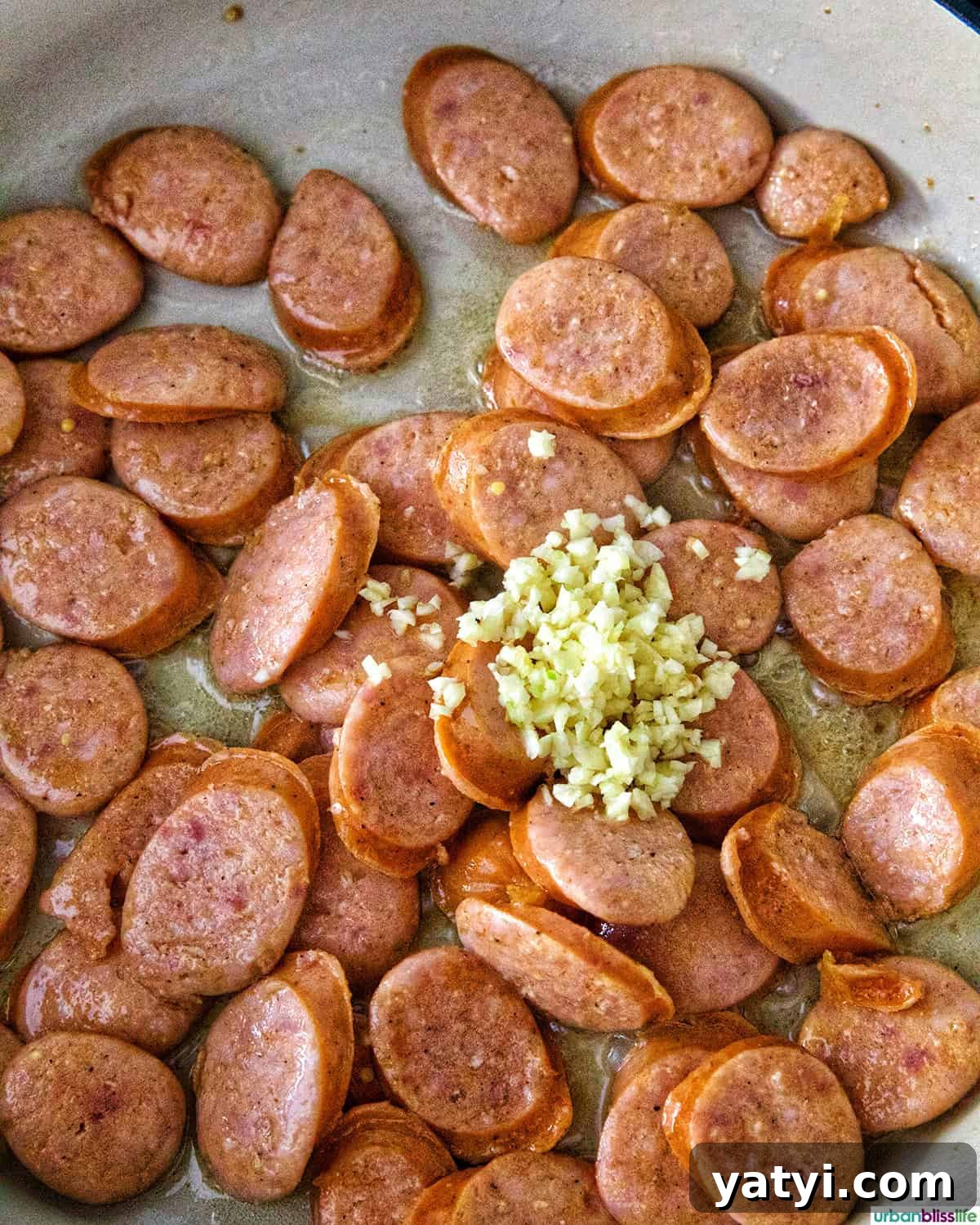Savory Sausage and Cabbage Skillet Recipe for Weeknight Dinners 8 minced garlic and sausage in a white pan.