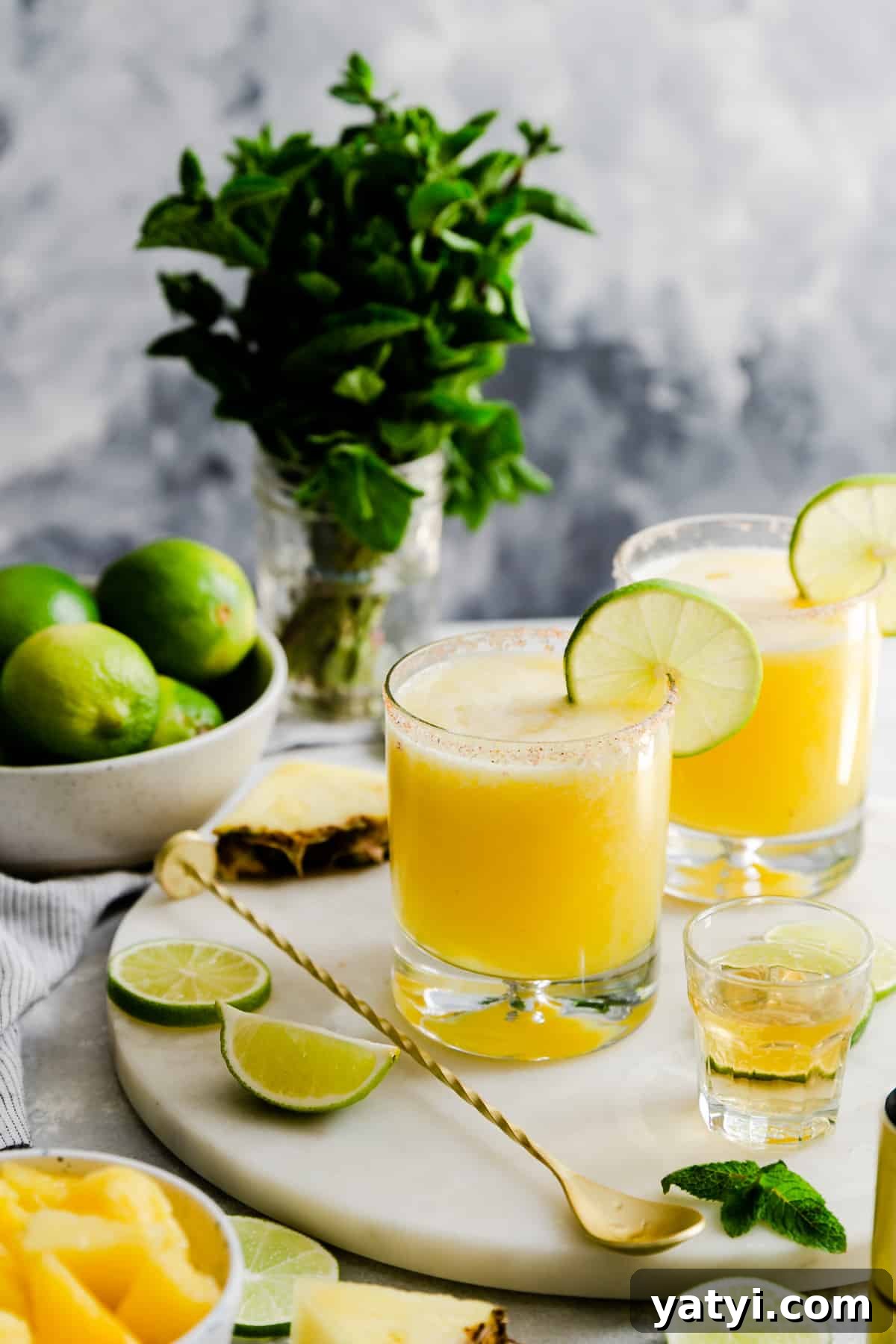 Frozen Pineapple Margarita Recipe — Tropical Cocktail Guide 2 two glasses with pineapple margaritas on a marble chopping board