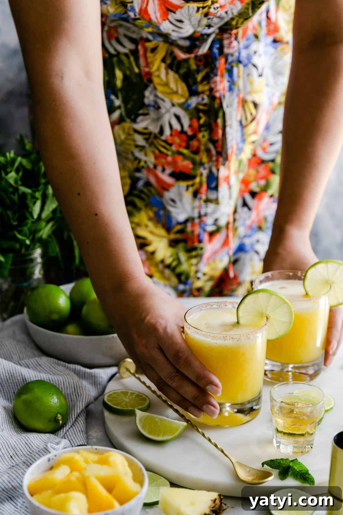 Frozen Pineapple Margarita Recipe — Tropical Cocktail Guide 7 a person holding two glasses of frozen pineapple margaritas