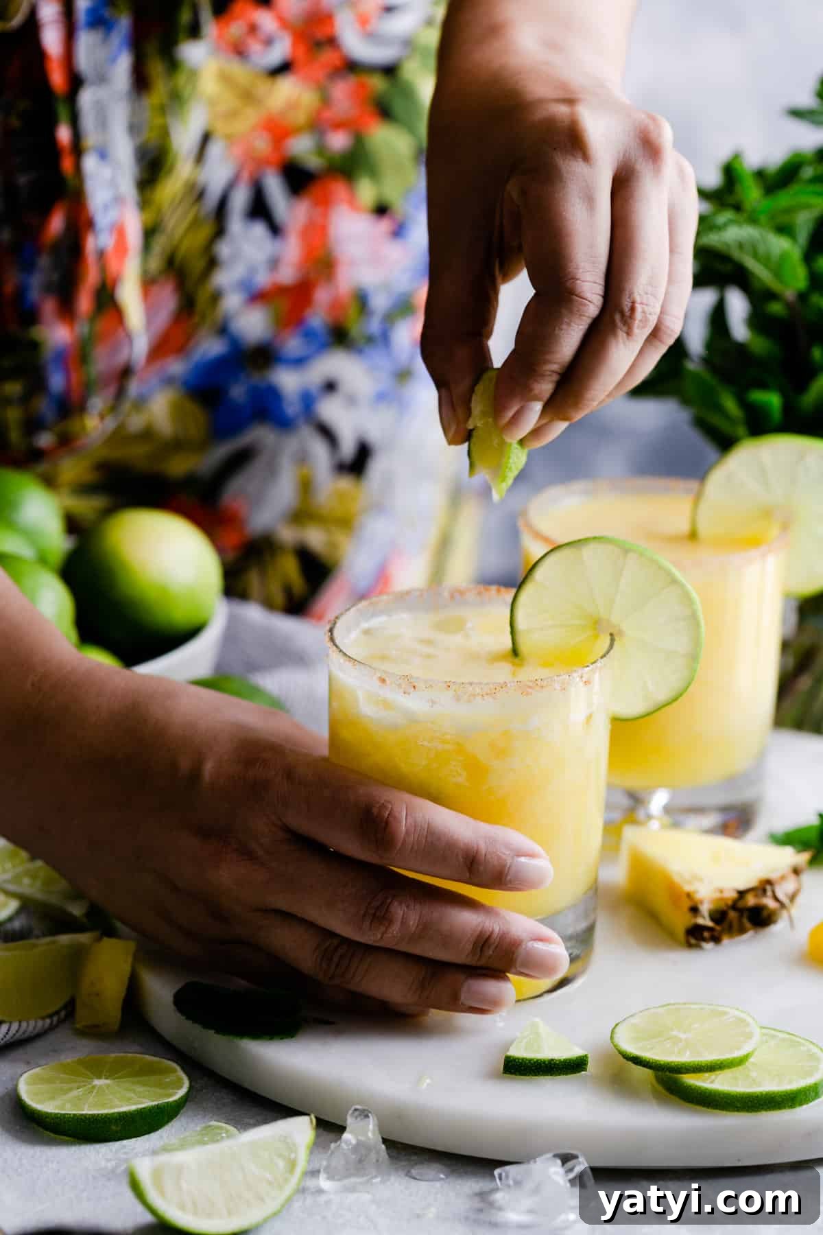 Frozen Pineapple Margarita Recipe — Tropical Cocktail Guide 9 a person squeezing a lime slice into a cocktail