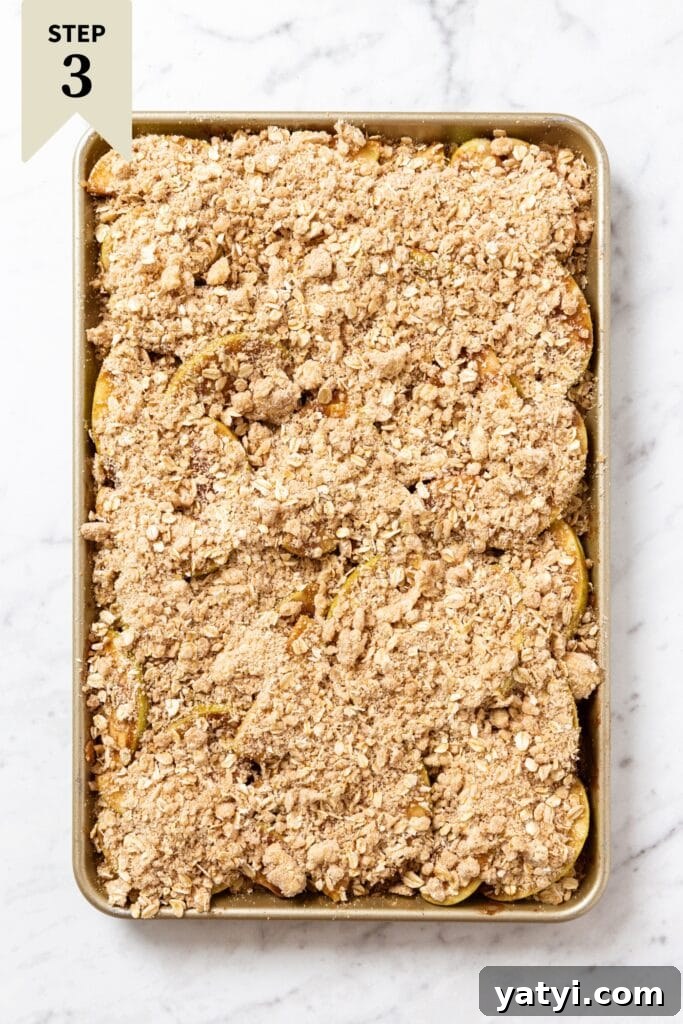 Chewy Cinnamon Apple Pie Bars: Easy Recipe for Fall Baking 15 White marble surface with gold baking sheet with apple pie bars covered in streusel topping before being baked.