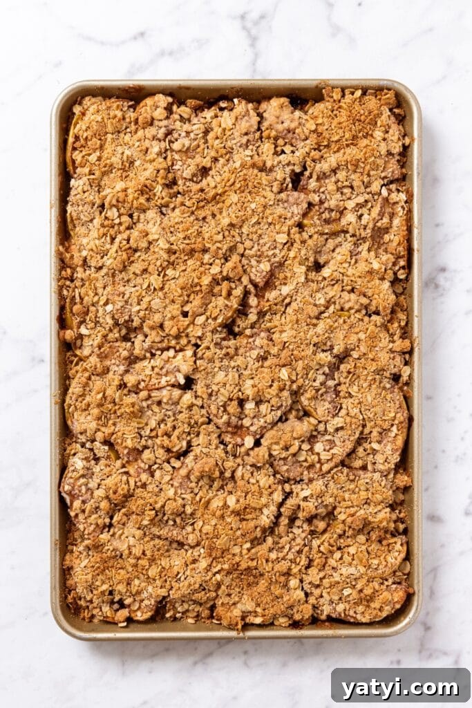 Chewy Cinnamon Apple Pie Bars: Easy Recipe for Fall Baking 16 Apple pie bars in gold baking pan right after being baked in the oven all on white marble surface.