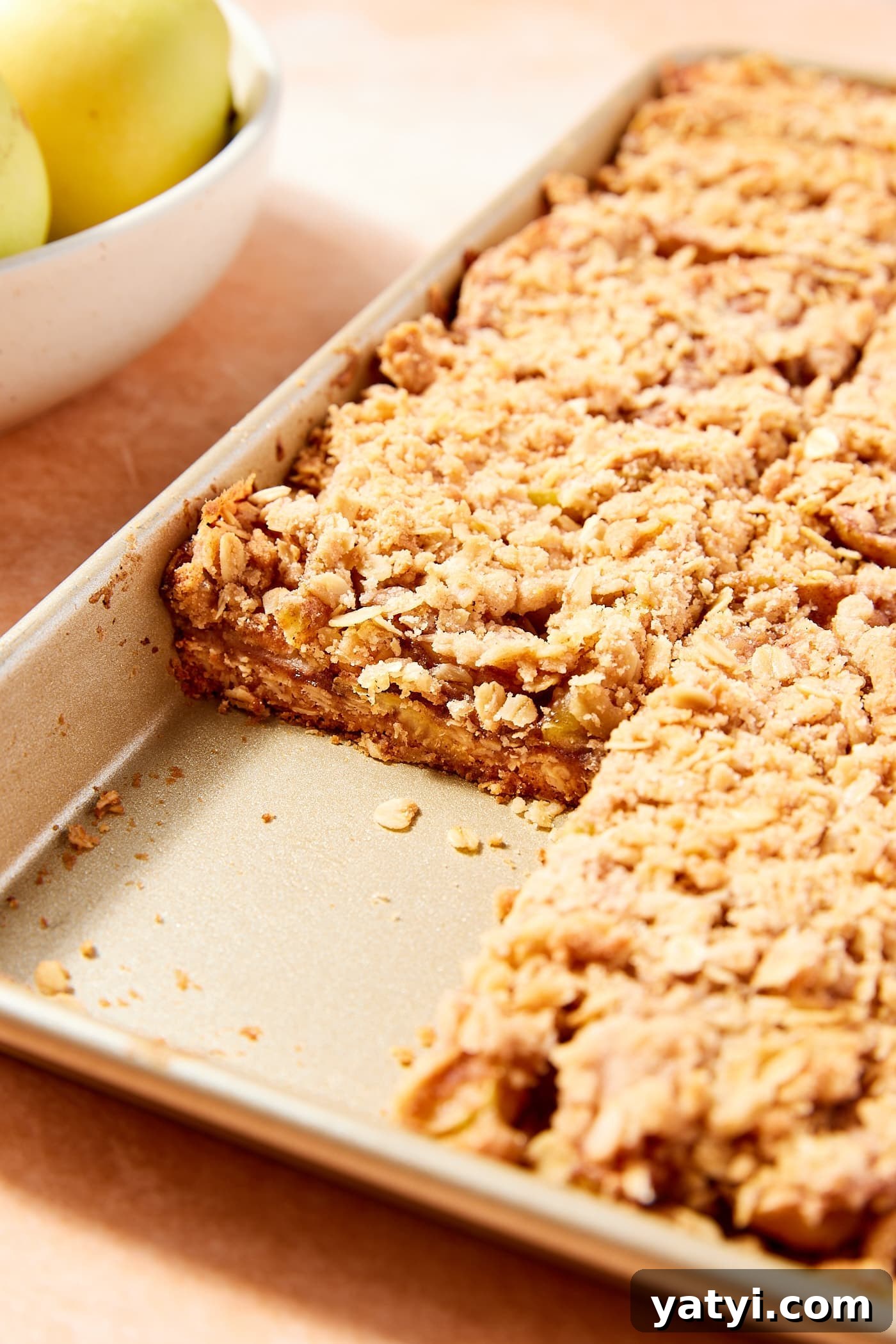 Chewy Cinnamon Apple Pie Bars: Easy Recipe for Fall Baking 17 Gold baking pan filled with apple pie bars with slices cut showing interior texture of the bars.