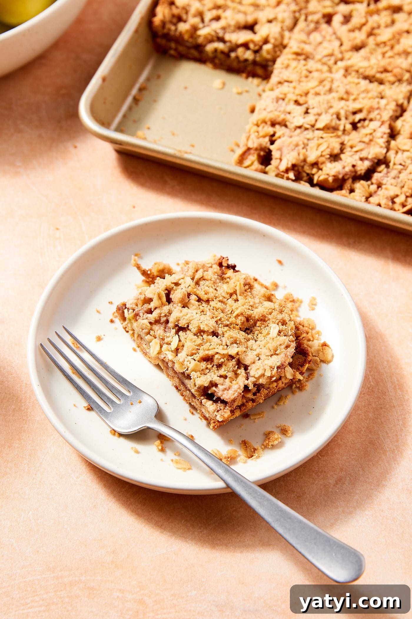 Chewy Cinnamon Apple Pie Bars: Easy Recipe for Fall Baking 18 White plate with slice of apple pie bar with fork resting to the side and remaining bars in the background.