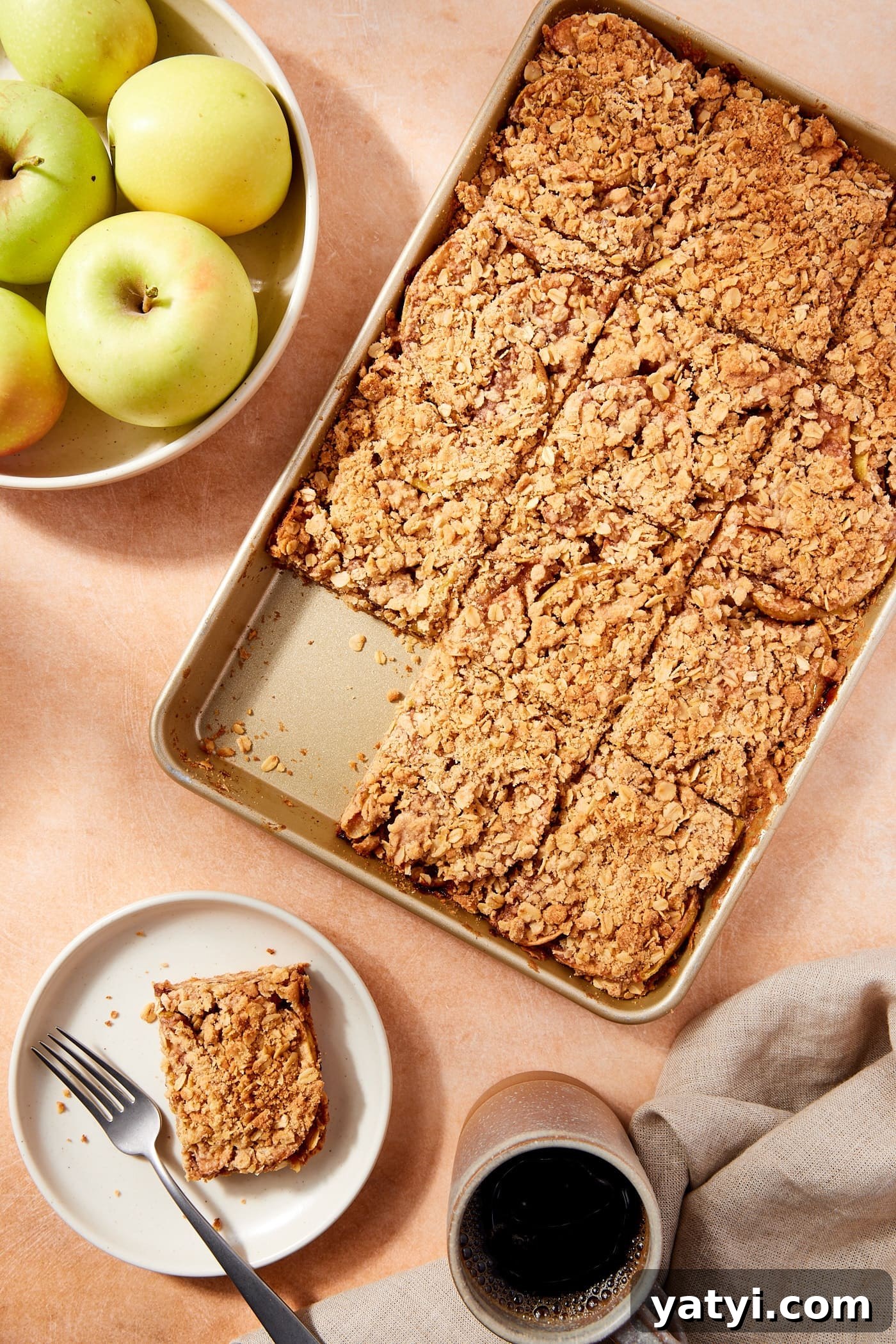 Chewy Cinnamon Apple Pie Bars: Easy Recipe for Fall Baking 3 Gold baking pan filled with baked apple pie bars sliced into rectangles with slice sitting on a white plate with bowl of apples.