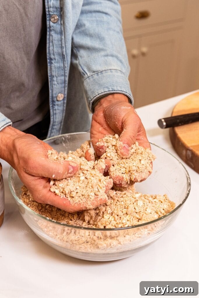 Chewy Cinnamon Apple Pie Bars: Easy Recipe for Fall Baking 8 Two hands crumbling together butter with oats and flour in a glass bowl for apple pie bars.