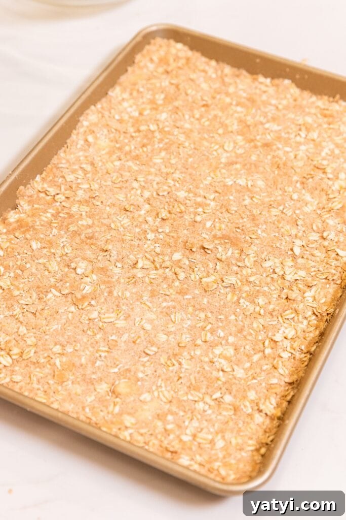 Chewy Cinnamon Apple Pie Bars: Easy Recipe for Fall Baking 10 Gold baking pan filled with crust made with oats and brown sugar sitting on white surface before going into the oven.