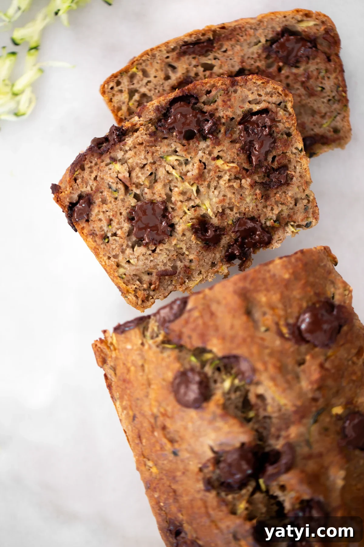 No-Added-Sugar Zucchini Banana Bread Recipe for Moist Loaves 2 Overhead shot of 2 slices of healthy zucchini banana bread with the rest of the loaf on a white marble background