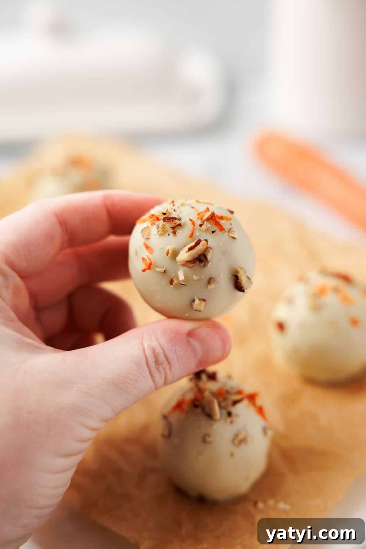Keto Carrot Cake Protein Bites Recipe for Low-Carb Snacks 11 Hand holding a white chocolate carrot cake bite topped with chopped pecans and shredded carrot