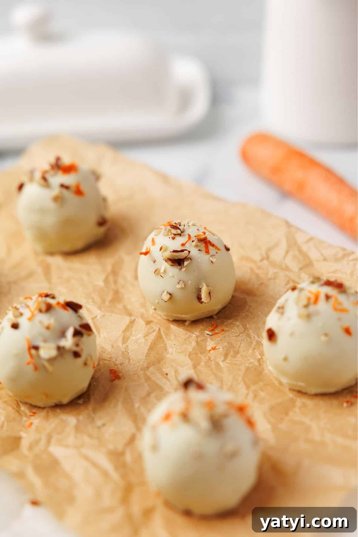 Keto Carrot Cake Protein Bites Recipe for Low-Carb Snacks 13 Six white chocolate carrot cake bites on parchment paper topped with pecans and shredded carrot, with a whole carrot in the background