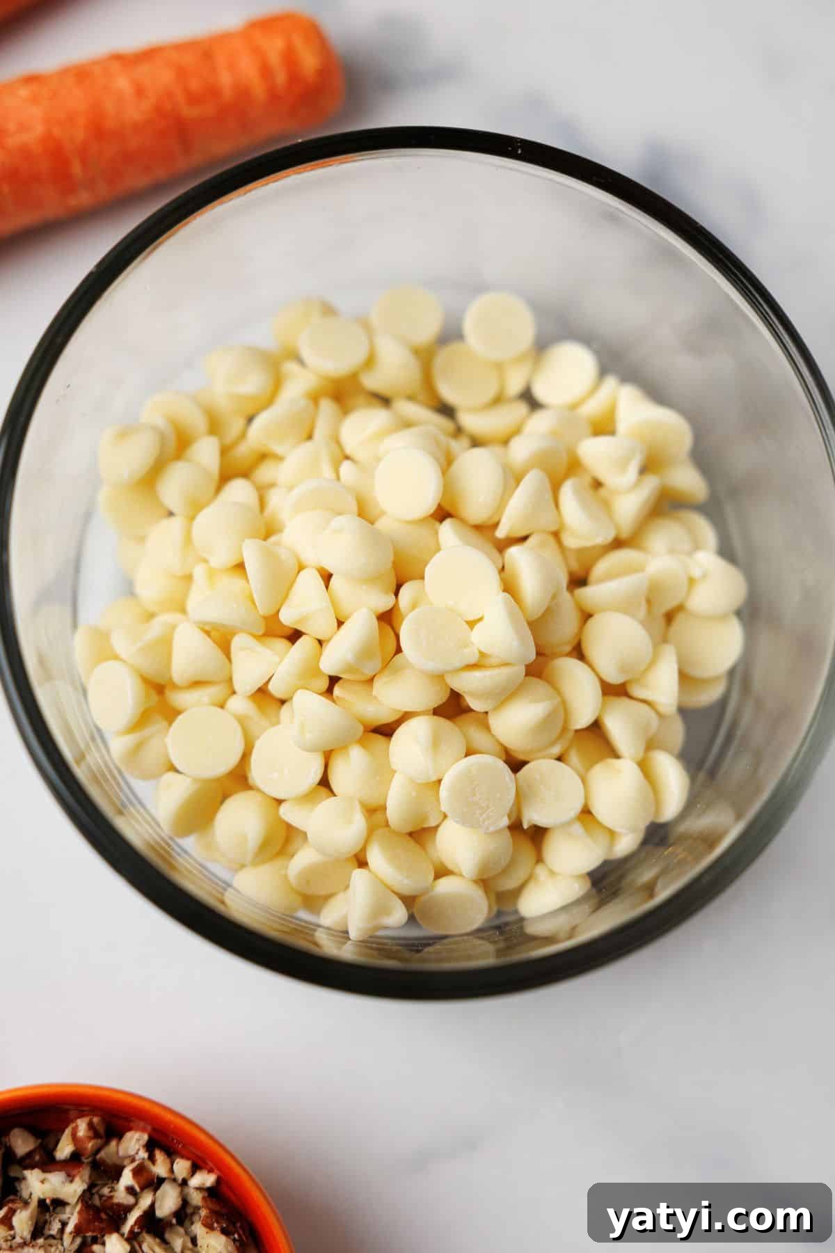 Keto Carrot Cake Protein Bites Recipe for Low-Carb Snacks 7 Sugar-free white chocolate chips in a glass bowl before melting, with a carrot and pecans nearby