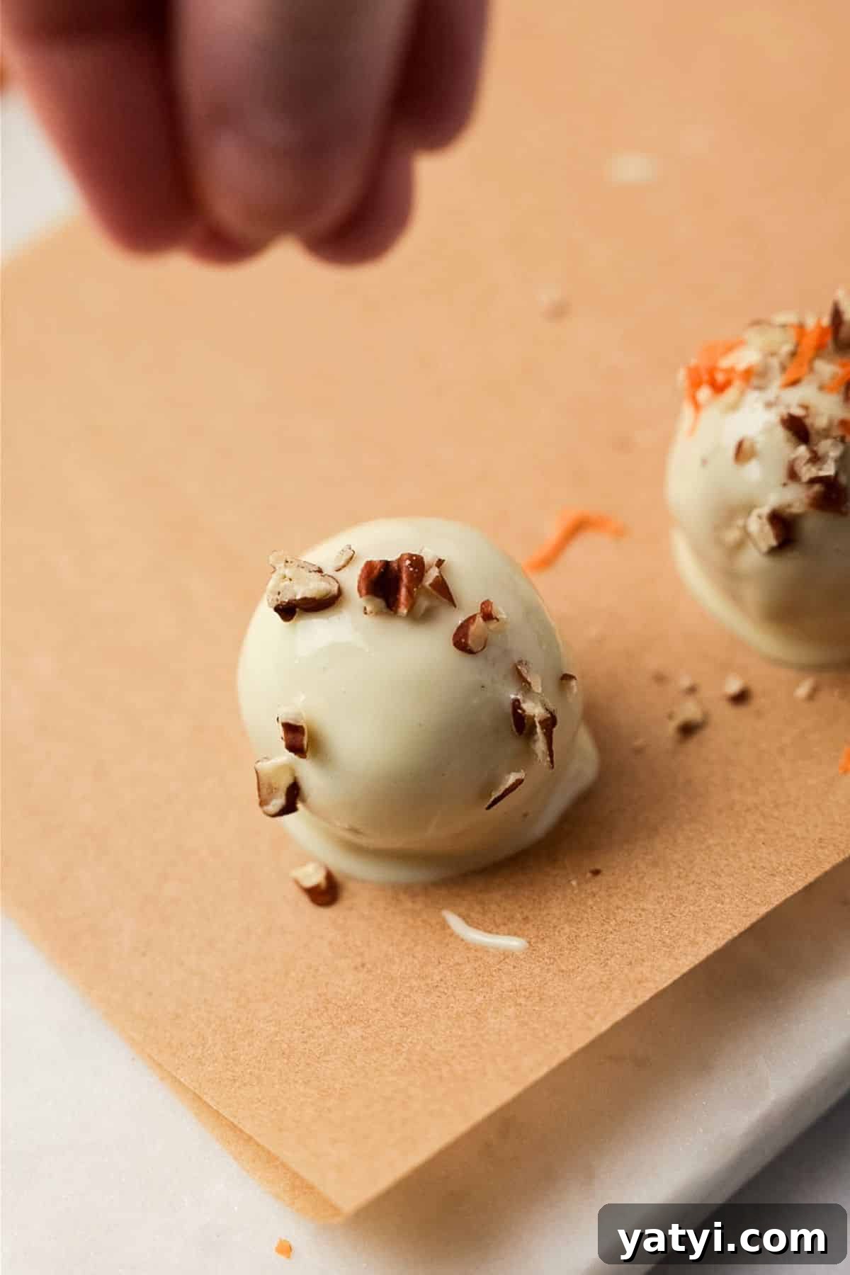 Keto Carrot Cake Protein Bites Recipe for Low-Carb Snacks 9 Hand sprinkling chopped pecans onto a freshly dipped white chocolate carrot cake bite