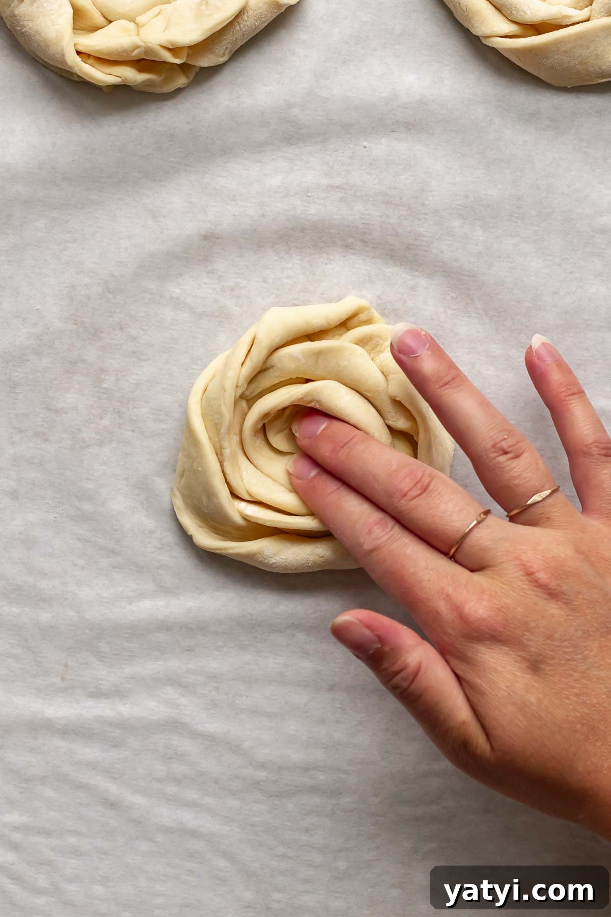 A hand presses down the middle of the puff pastry coil.