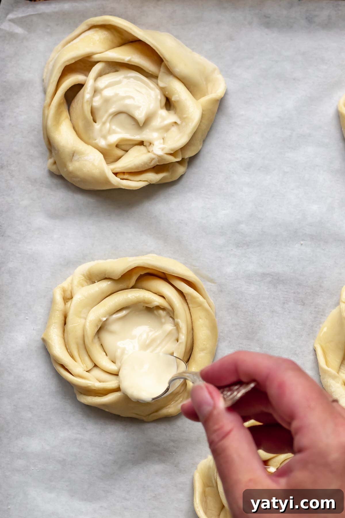 A hand adds cream cheese mixture to the center of the puff pastry roses.