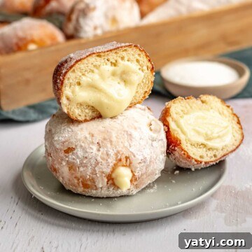 Custard donuts stacked on a plate. The top one is cut open to show the pastry cream coming out.