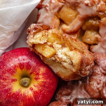 A basket of apple fritter donuts next to an apple. One it broken open.
