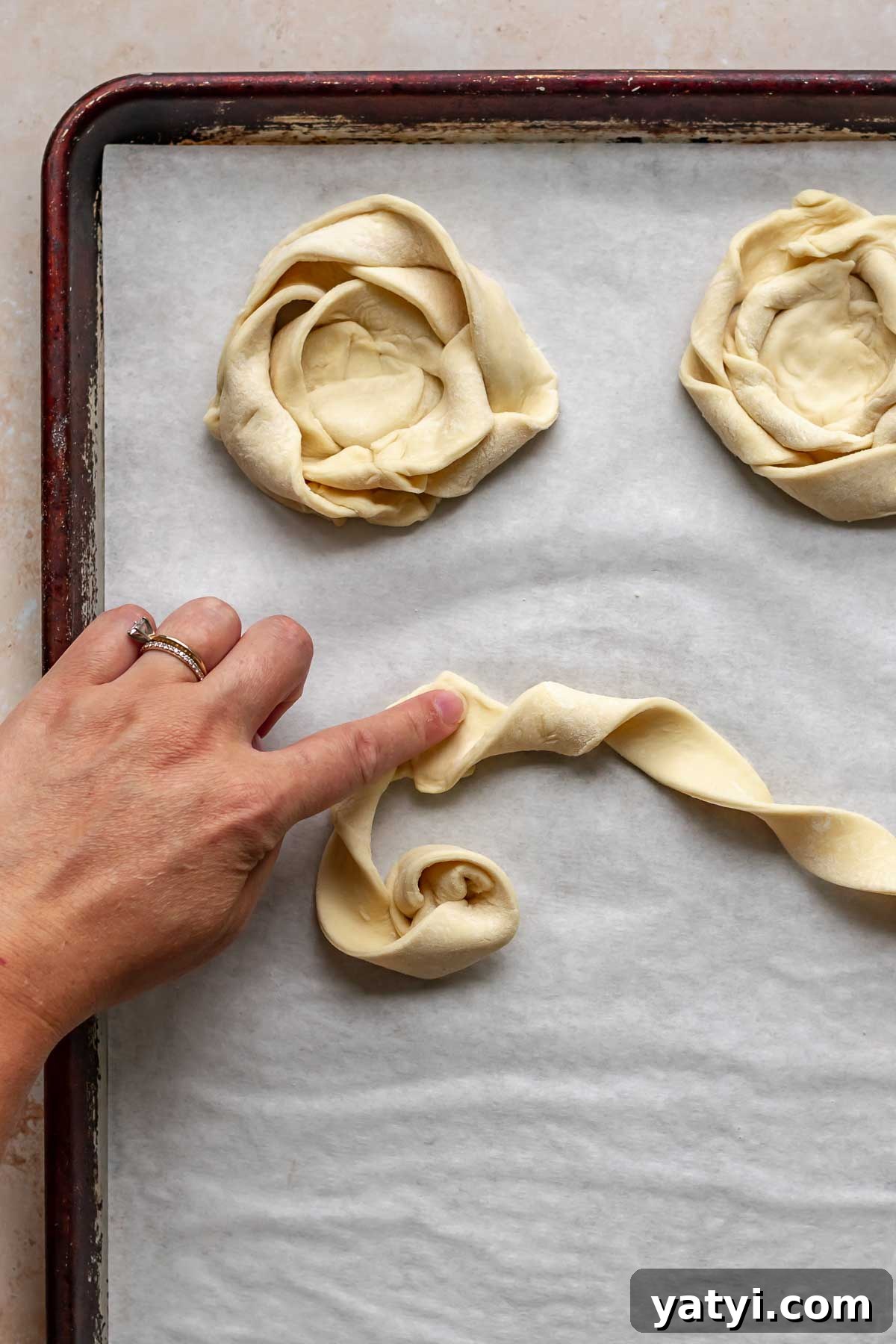 A hand presses together two strips of coiled puff pastry.