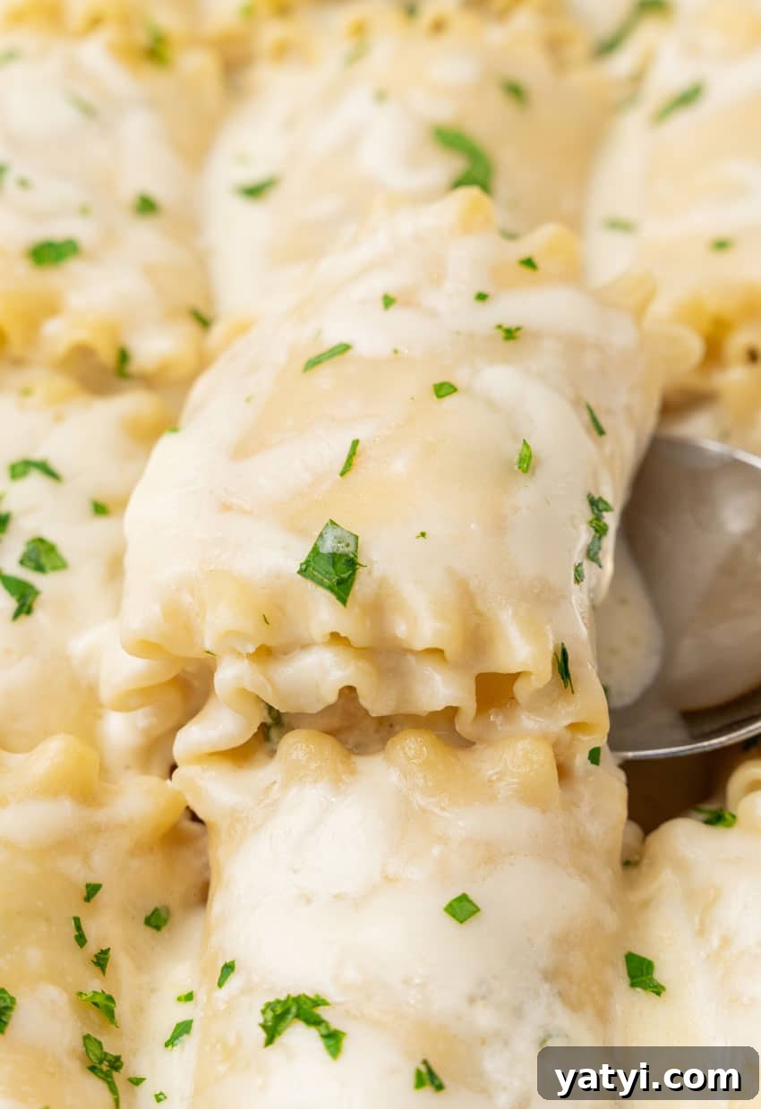 Creamy White Chicken Lasagna Roll-Ups for Family Dinner 11 a silver spoon scooping a white chicken lasagna roll up out of a white baking dish