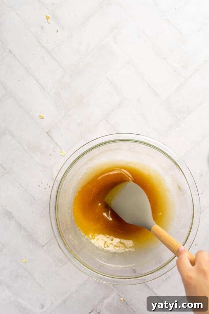 Homemade Gluten-Free Granola Bars with Oats and Almonds 4 A hand holding a spatula mixing honey and butter