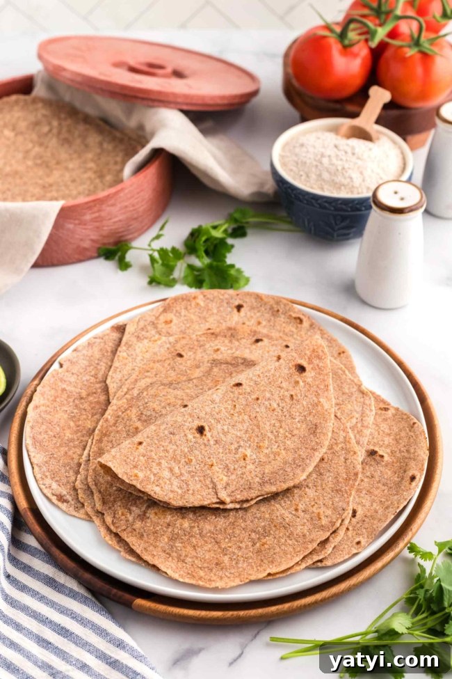 Homemade Whole Wheat Tortillas: Soft, Flexible Wraps Recipe 2 white plated filled with whole wheat tortillas with tortilla warmer in background on a white table
