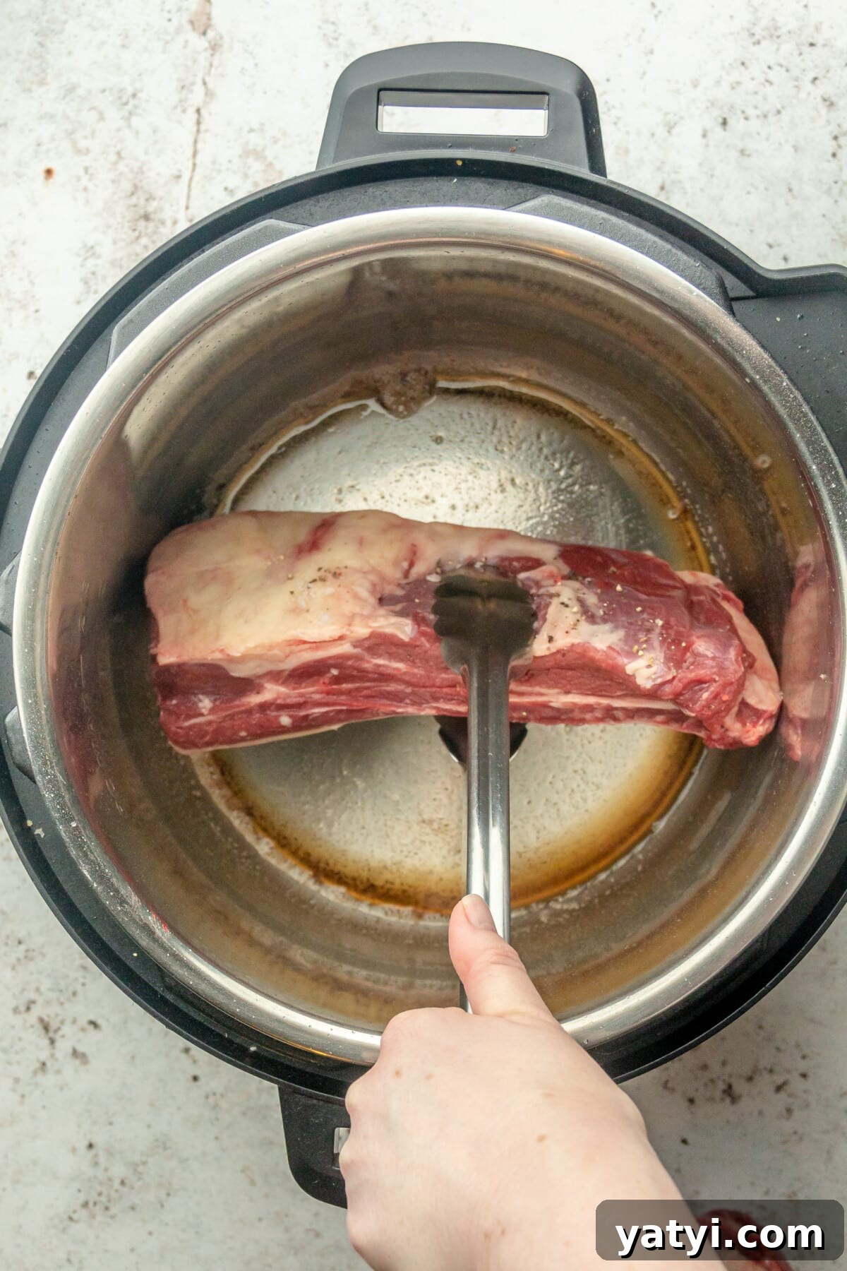 Rustic Instant Pot Short Ribs Recipe — Tender Braised Beef 4 Short ribs are placed into an instant pot on a light gray surface.