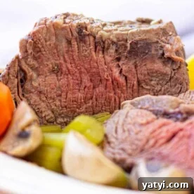 How to Roast a Tender Cross Rib Roast Perfectly 4 Close-up of a sliced Cross Rib Roast with tender carrots, potatoes, and mushrooms on a plate.