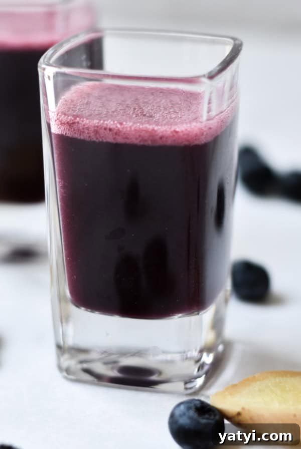 Ginger Juice Recipe: Make Fresh Ginger Juice with a Blender or Juicer 11 Immunity shots on a marble background with fresh ginger sliced next to the glasses.