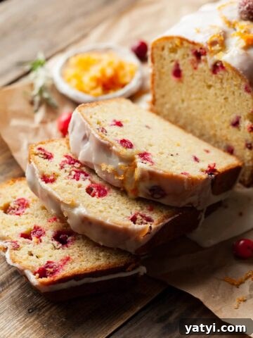 slices of cranberry orange bread topped with orange glaze, small bowl of sugared orange zest, fresh cranberries and a spring of rosemary