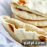 Gluten-Free Pita Bread Recipe: Soft, Flavorful, and Simple 9 stack of gf pita bread on white towel with one cut in half to show pocket.