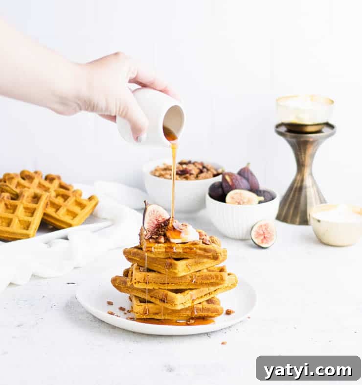 Fluffy Buttermilk Pumpkin Waffles Recipe for Fall Breakfast 2 four orange pumpkin waffles stacked on top of each other with a fig, granola and butter with maple syrup poured over the top from a small white pitcher.