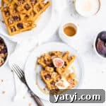 two triangles of waffles on a blue plate topped with a square of butter, a halved fig and granola.