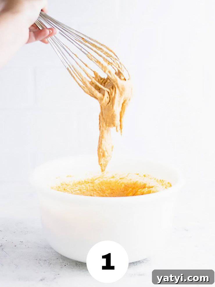 Fluffy Buttermilk Pumpkin Waffles Recipe for Fall Breakfast 3 Whisk with thick, orange batter dripping off of it into a white bowl.