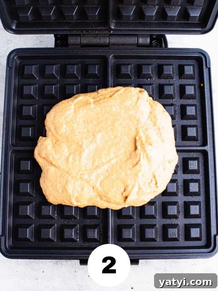 Fluffy Buttermilk Pumpkin Waffles Recipe for Fall Breakfast 4 Overhead view of light orange waffle batter on a black waffle iron.