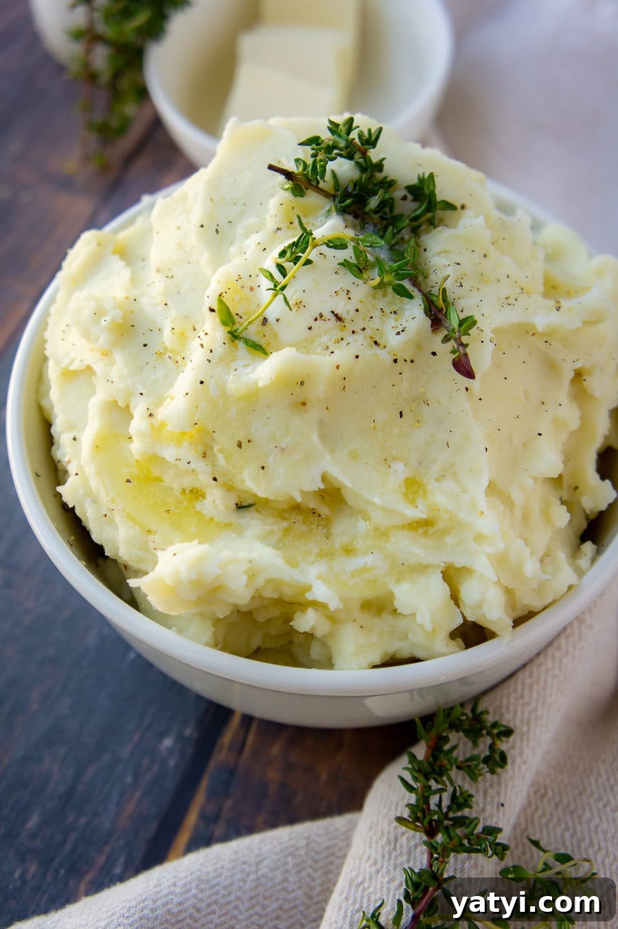 a bowl of creamy mashed potatoes with fresh thyme and butter on top.