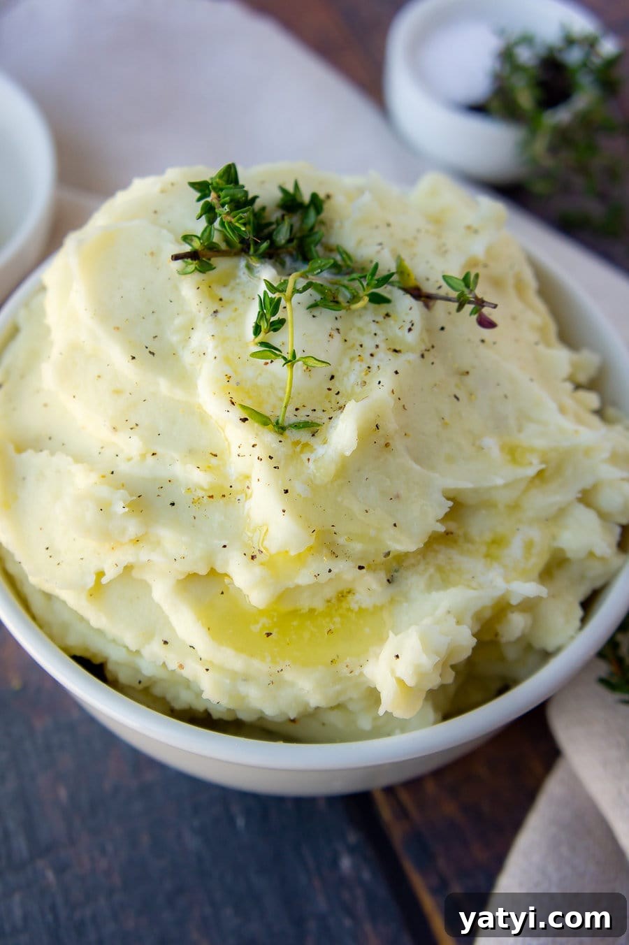 a bowl of mashed potatoes topped with butter, pepper, and fresh thyme sprigs.