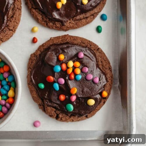 Cookies covered in chocolate ganache and rainbow chips on parchment paper.