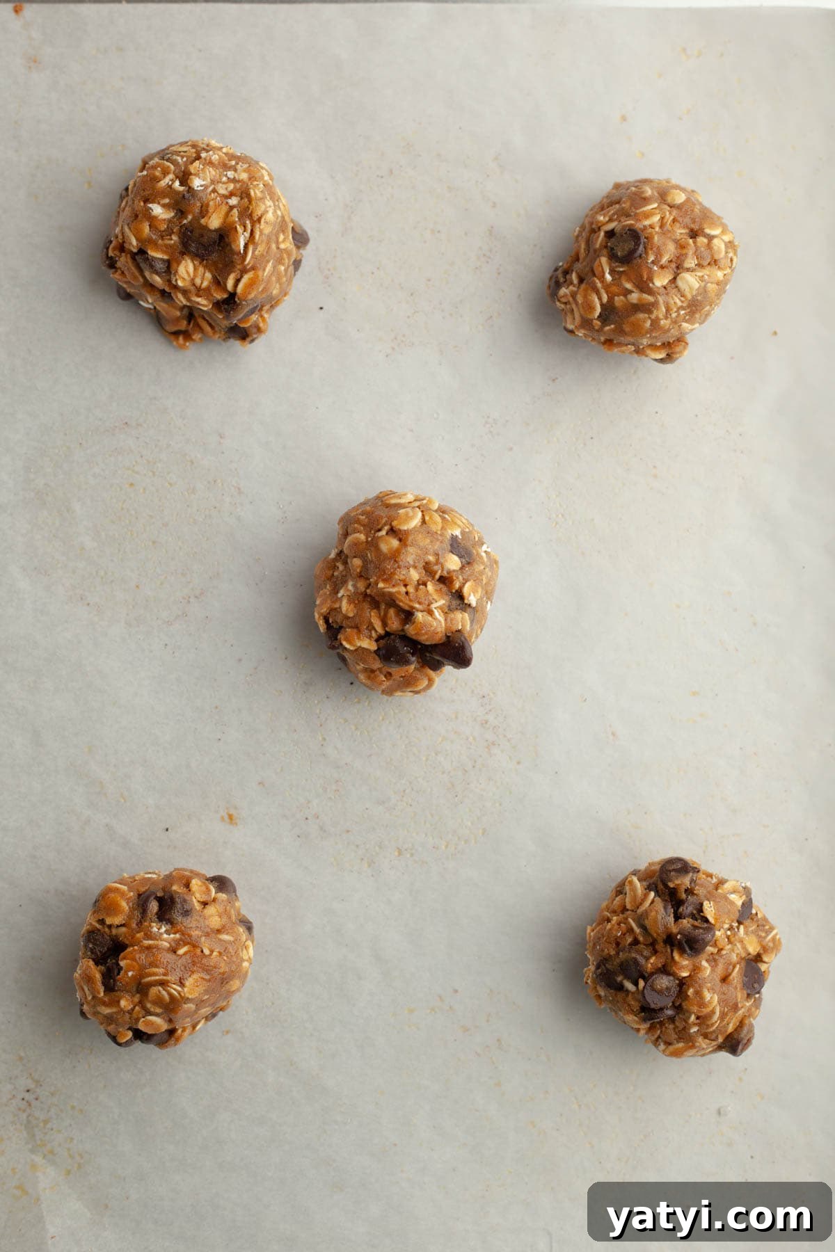 Chewy Brown-Butter Oatmeal Cookies with Chocolate Chips 9 Unbaked oatmeal chocolate chip cookie dough balls on parchment paper.