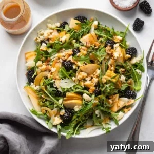 arugula salad in a white bowl with pears, walnuts, gorgonzola, and blackberries.