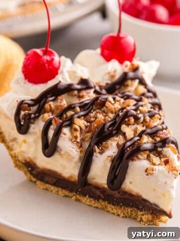 Slice of banana split pie topped with whipped cream, chopped pecans, chocolate syrup, and cherries.