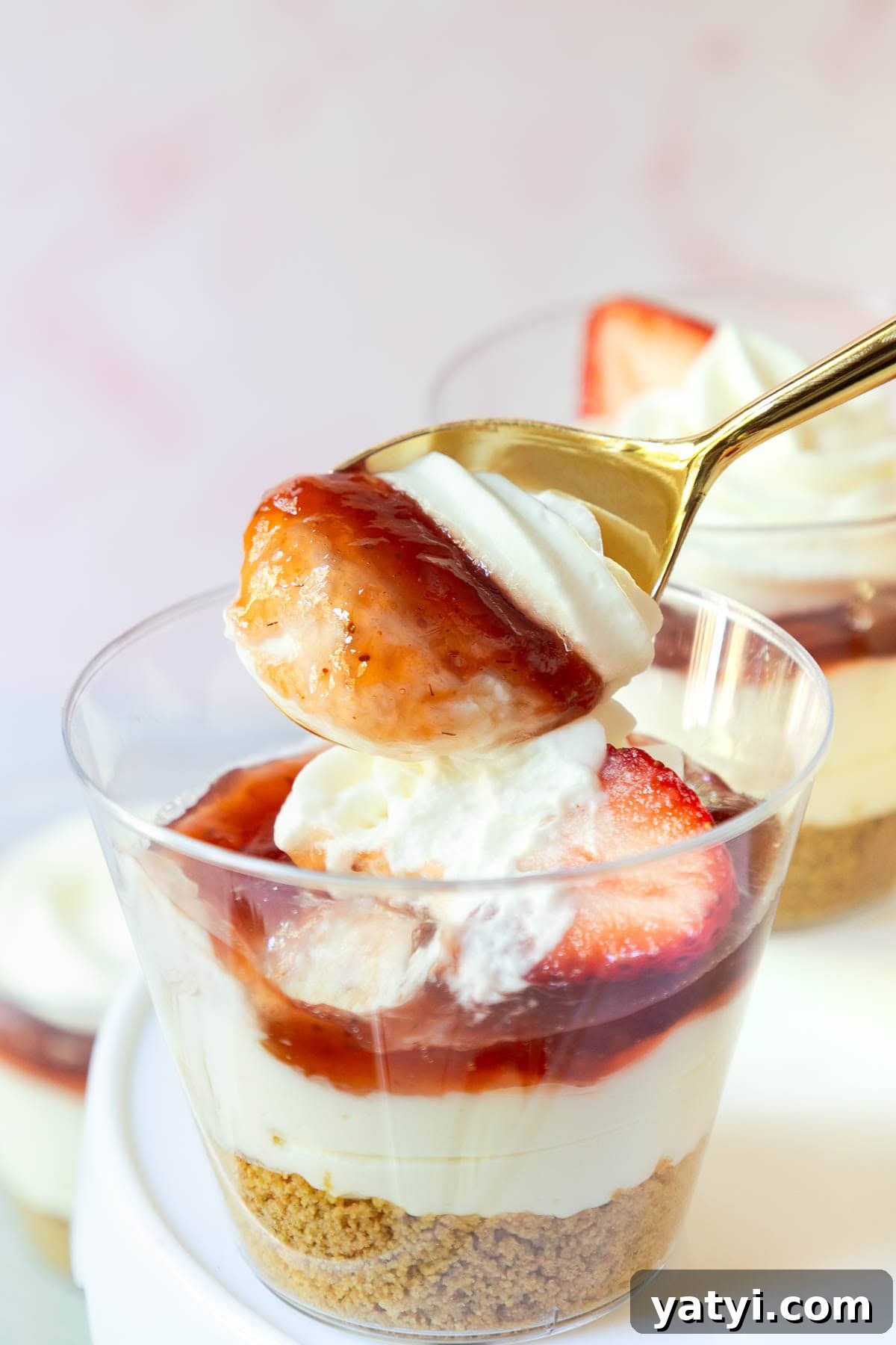 No-Bake Strawberry Cheesecake Cups with Graham Cracker Crust 10 A spoon lifting a bite of strawberry cheesecake from a cup, showing layers of cream, jam, and sliced strawberry.