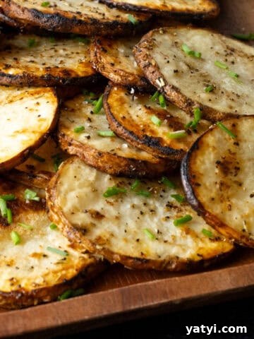 Stack of sliced thinly grilled potatoes on wooden serving platter.