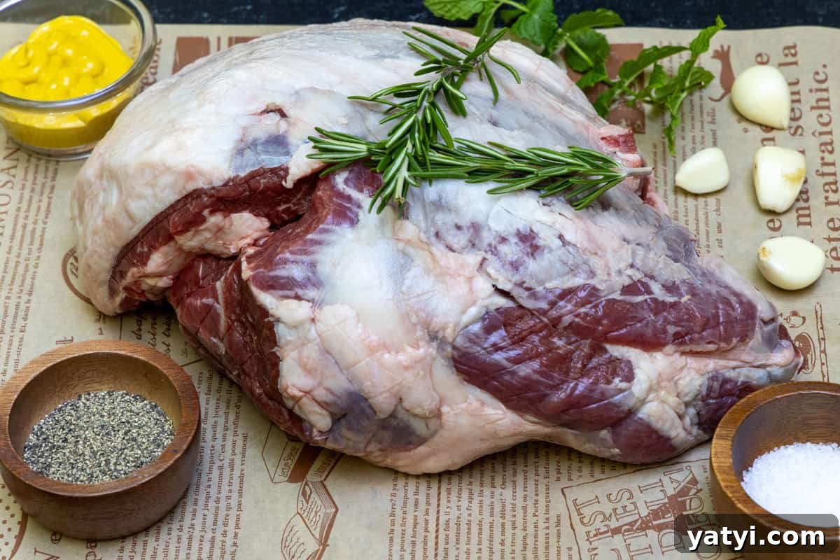 Juicy Smoked Leg of Lamb Recipe for Tender, Flavorful Roast 3 Leg of lamb on cutting board with pepper, mustard, salt, and garlic cloves surrounding meat.